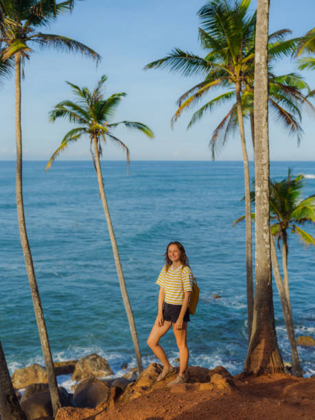 A woman stands on a rock surrounded by palm trees in Mirissa, showcasing a tropical coastal landscape.