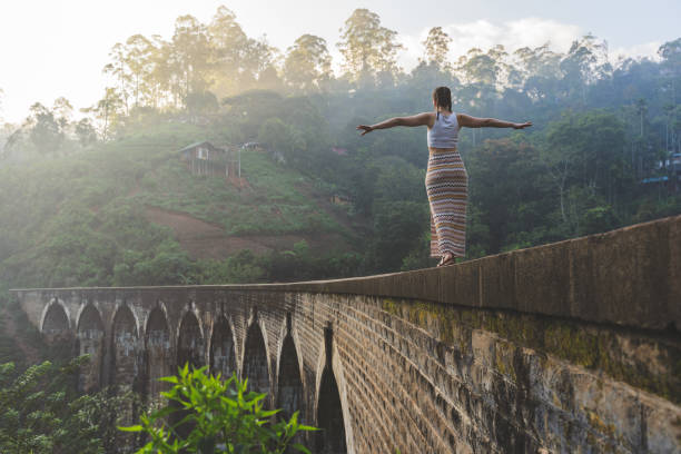 A woman with outstretched arms stands on a bridge, symbolizing openness and connection to her surroundings.