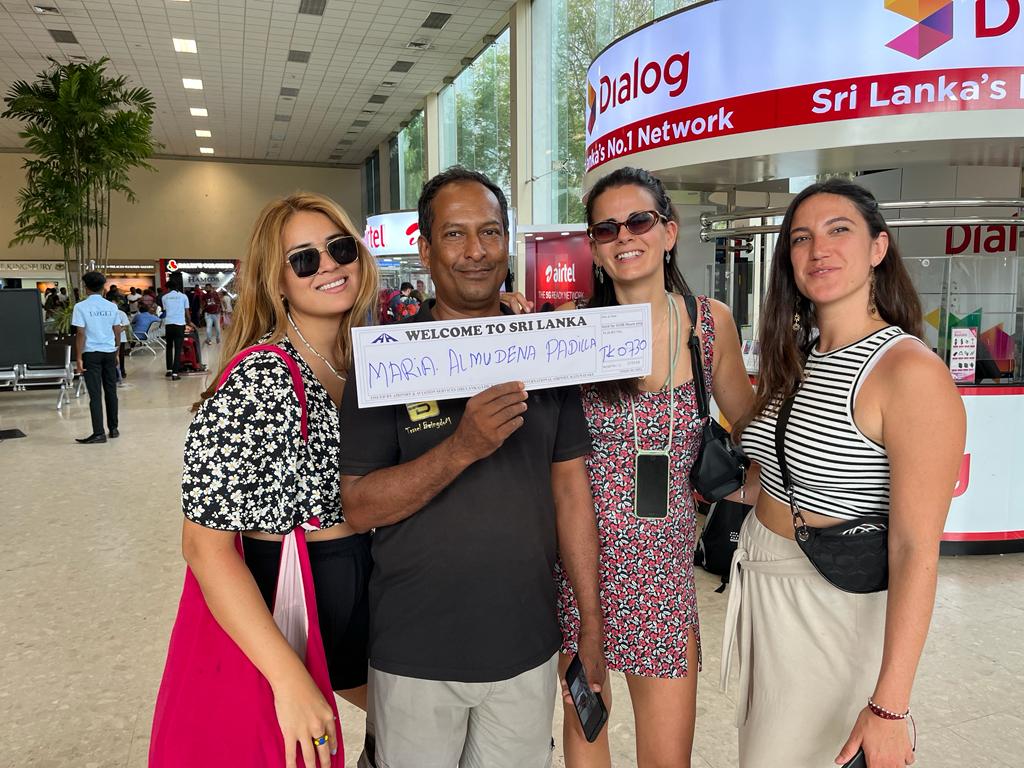 A group of three women and one man smiles for a photo at an airport in Sri Lanka, ready for their transfer.