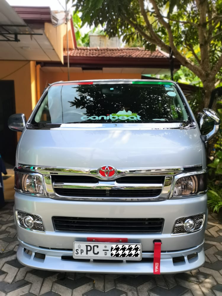 A white van parked along the roadside, surrounded by greenery and a clear blue sky.