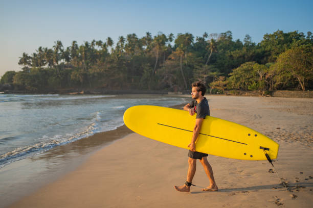 A man stands on the beach, holding a vibrant yellow surfboard, ready for a day of surfing in the sun.