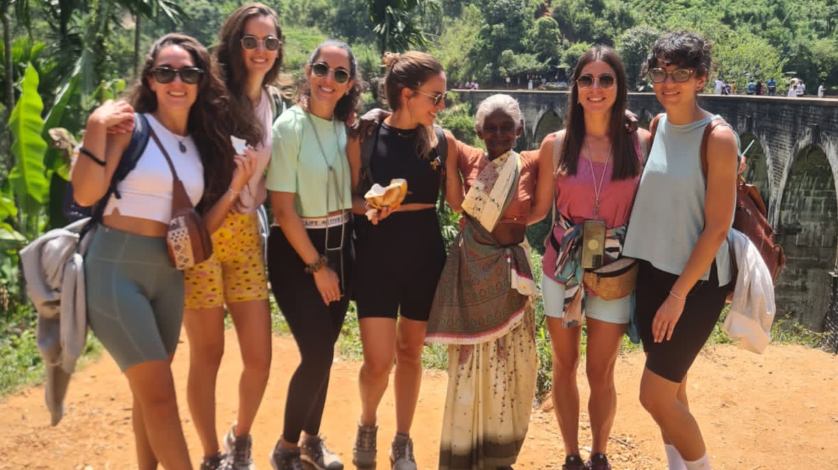 A group of women smiling and posing together on a dirt road, capturing a memorable moment during their day tour.